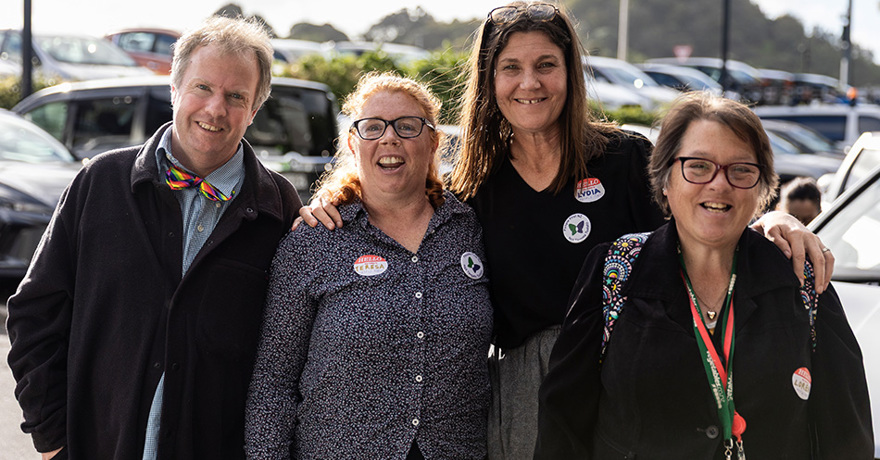 Four people smiling together outdoors in a parking lot, wearing "Hello My Name Is" name tags (Teresa, Lydia, and Lorene) and event badges.