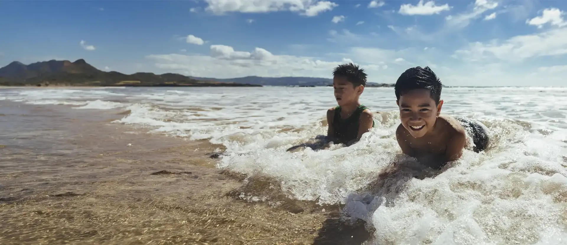 Two smiling children playing in foaming ocean waves on a sunny beach. (1)