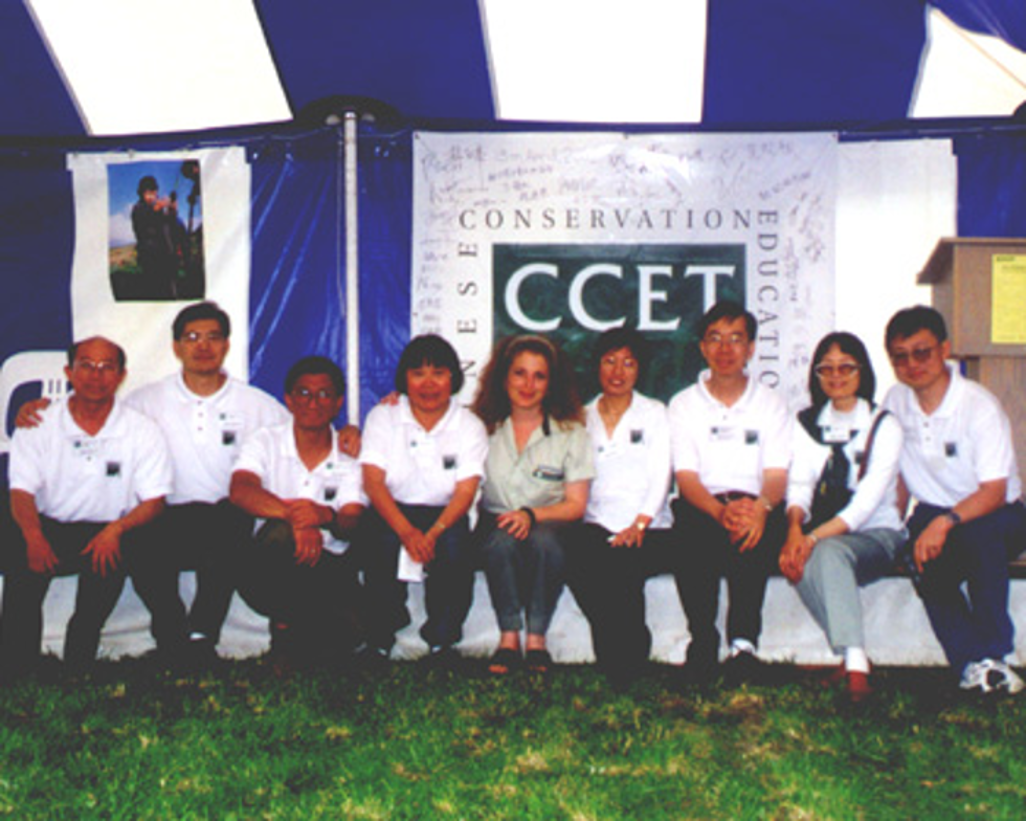 A group of nine people sits together in front of a "Chinese Conservation Education Trust" banner under a marquee tent.